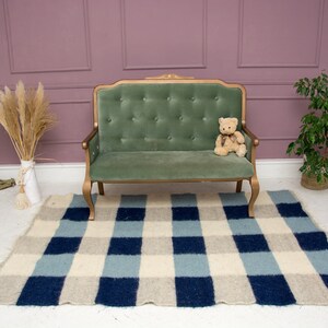 May include: A green velvet tufted sofa with gold-painted legs sits on a blue and white checked rug in a room with a pink wall and a potted plant.