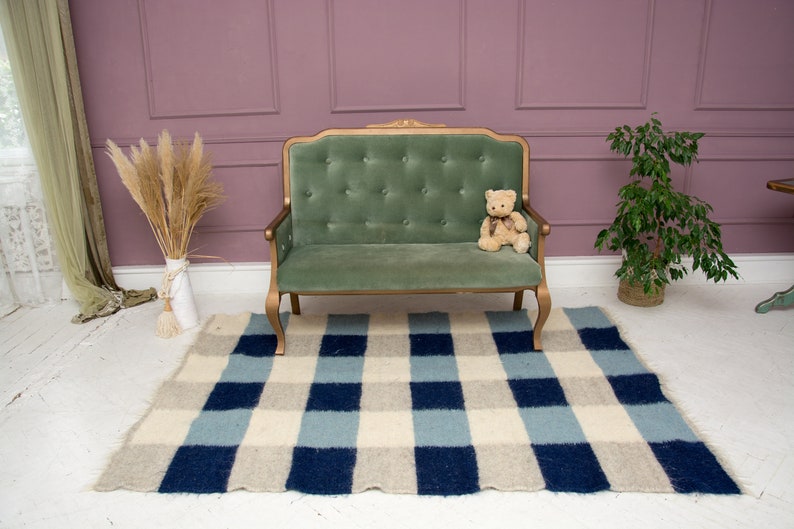 May include: A green velvet tufted sofa with gold-painted legs sits on a blue and white checked rug in a room with a pink wall and a potted plant.