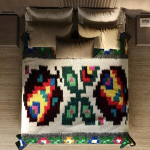Pu&ograve; includere: Un letto bianco con una coperta a motivi colorati. La coperta presenta un design geometrico con accenti rossi, gialli, verdi e blu. Il letto &egrave; fatto con cuscini bianchi e un cuscino a righe marroni.