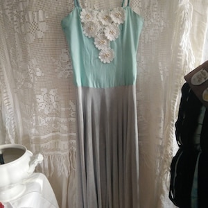 May include: A light blue and gray sleeveless dress with a white floral embellishment on the bodice.