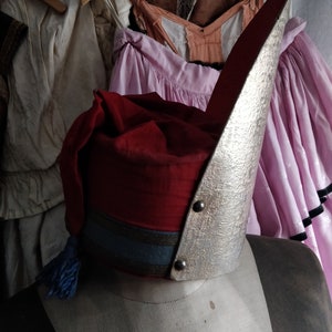 May include: A red and silver hat with a blue tassel. The hat is on a mannequin with a white fabric background.