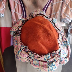 May include: A red felt hat with a patterned fabric trim. The hat is round and has a flat top.