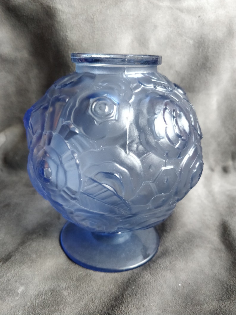 Op de afbeelding: Een blauwe glazen vaas met een rond lichaam en een voet. De vaas is versierd met een reli&euml;f van rozen.