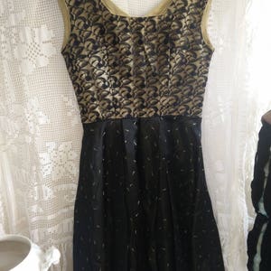 May include: A black and gold sleeveless dress with a fitted bodice and a full skirt. The bodice has a black lace pattern on a gold background. The skirt has a black background with gold accents.