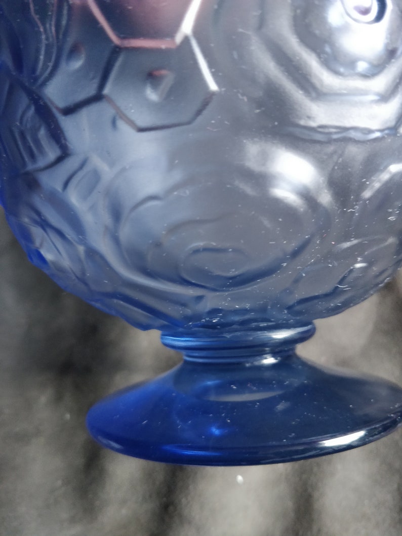 Op de afbeelding: Een blauwe glazen beker met een getextureerd, reli&euml;fdesign. De beker heeft een brede basis en een ronde kom.