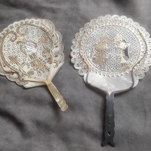 May include: Two ornate, hand-painted, white fans with intricate designs. One fan has a black handle and the other has a white handle.