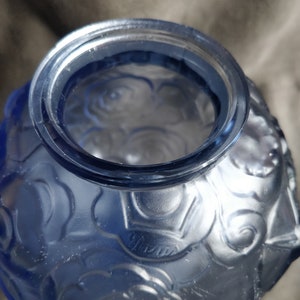 Op de afbeelding: Een blauwe glazen vaas met een getextureerd rozenpatroon. De vaas heeft een brede opening en een ronde vorm.