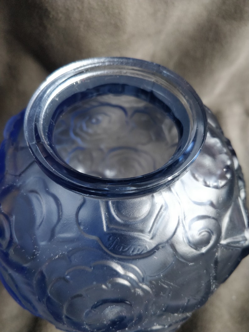Op de afbeelding: Een blauwe glazen vaas met een getextureerd rozenpatroon. De vaas heeft een brede opening en een ronde vorm.