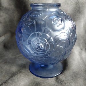 Op de afbeelding: Een blauwe glazen vaas met een rond lichaam en een brede basis. De vaas is versierd met een herhalend patroon van ge&euml;mbosseerde bloemen.