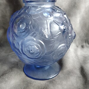 Op de afbeelding: Een blauwe glazen vaas met een rond lichaam en een brede basis. De vaas is versierd met een bloemenpatroon.