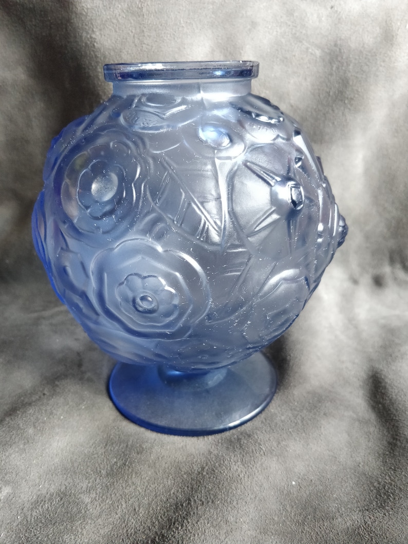 Op de afbeelding: Een blauwe glazen vaas met een rond lichaam en een brede basis. De vaas is versierd met een bloemenpatroon.