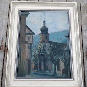 Könnte beinhalten: Ein gerahmtes Ölgemälde, das eine Kirche mit einem hohen Kirchturm und einer Reihe von Bäumen davor zeigt. Das Gemälde ist vor einem blauen Himmel mit weißen Wolken platziert. Die Unterschrift des Künstlers ist in der unteren rechten Ecke sichtbar.
