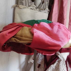 May include: A multi-colored hat made of fabric. The hat is pink, brown, green, and red. The hat is on a stand.