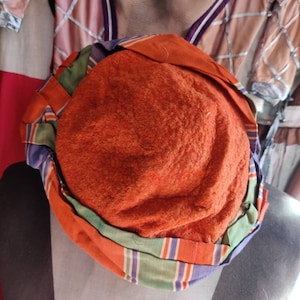 May include: A round, orange hat with green, blue, and white stripes. The hat is made of a soft, fuzzy material.