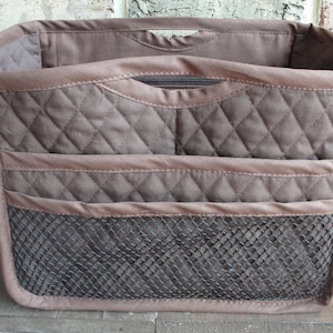 May include: A brown quilted organizer bag with a zippered top and a mesh bottom compartment. The bag has multiple pockets and compartments for organizing items.