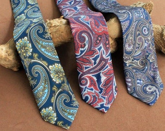 Pode incluir: Três gravatas com padrão paisley em azul, vermelho e roxo. As gravatas estão dispostas sobre uma superfície marrom.