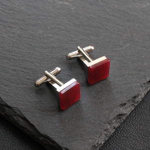 May include: A pair of silver cufflinks with square red gemstone accents.
