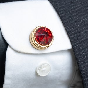 以下が含まれることがあります： 中央に赤いファセットカットの宝石がついた金の袖口ボタン