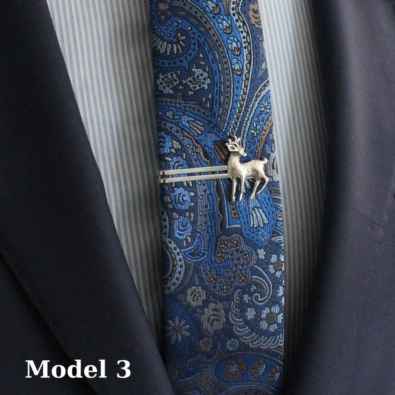 May include: A blue paisley patterned tie with a silver deer tie clip. The tie is worn with a navy blue suit jacket and a striped dress shirt. The text "Model 3" is visible in the lower left corner.