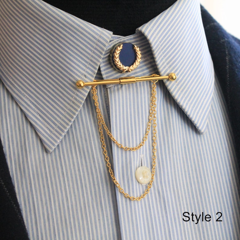 Pode incluir: Barra de colarinho dourada com um detalhe azul e dourado e correntes penduradas. A barra est&aacute; presa a uma camisa listrada azul e branca. Um pequeno bot&atilde;o branco est&aacute; na extremidade das correntes. O texto "Style 2" &eacute; vis&iacute;vel.