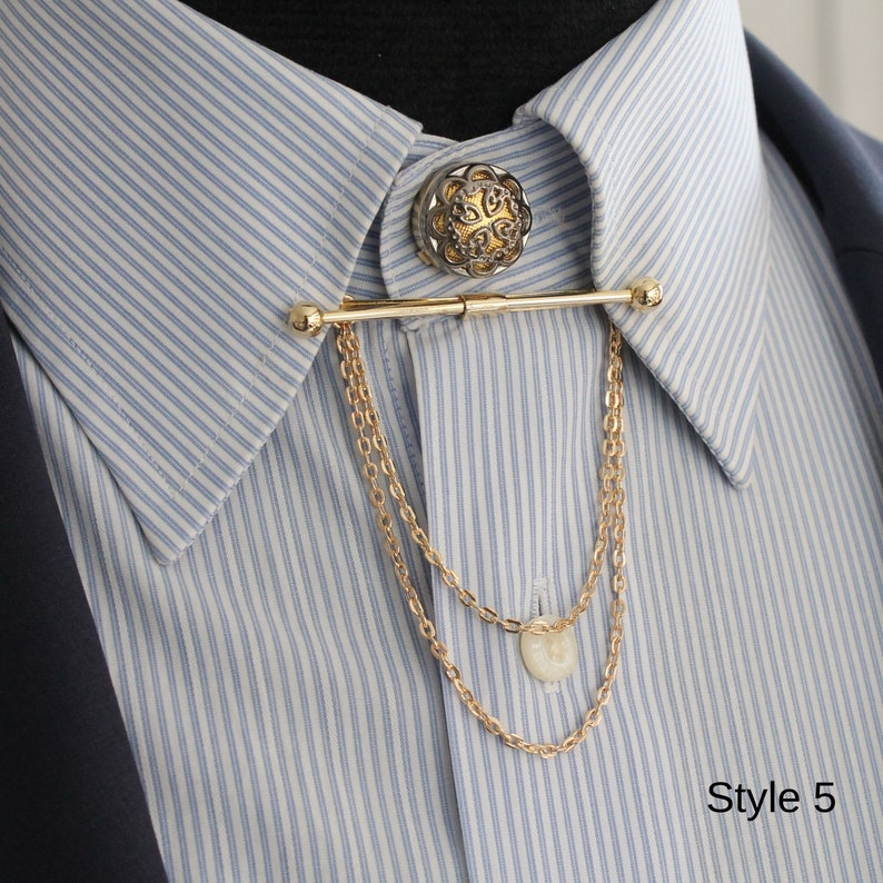 Pode incluir: Barra de colarinho dourada com um bot&atilde;o decorativo e detalhe de corrente, mostrada em uma camisa listrada azul e branca. O bot&atilde;o tem um design ornamentado. O texto "Style 5" &eacute; vis&iacute;vel na imagem.