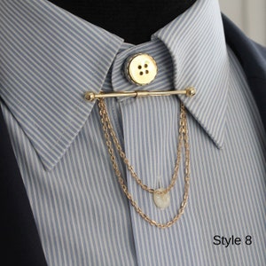 Pode incluir: Uma barra de colarinho dourada com bot&atilde;o e detalhe de corrente, mostrada numa camisa listrada azul e branca. A barra &eacute; presa a um bot&atilde;o na gola e pende com duas correntes delicadas. O texto "Style 8" est&aacute; no canto inferior direito.