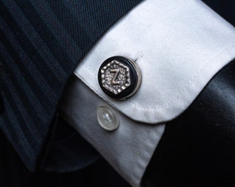 May include: A black and silver cufflink with a hexagonal design and the letter 'Z' in the center.