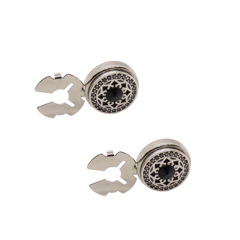 May include: A pair of silver-toned shirt fasteners with a black center stone and an intricate design. Each fastener has a clip on the back.
