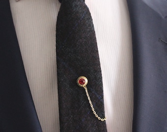 May include: A dark blue patterned tie with a gold tie tack featuring a red gemstone. The tie tack has a chain attached.