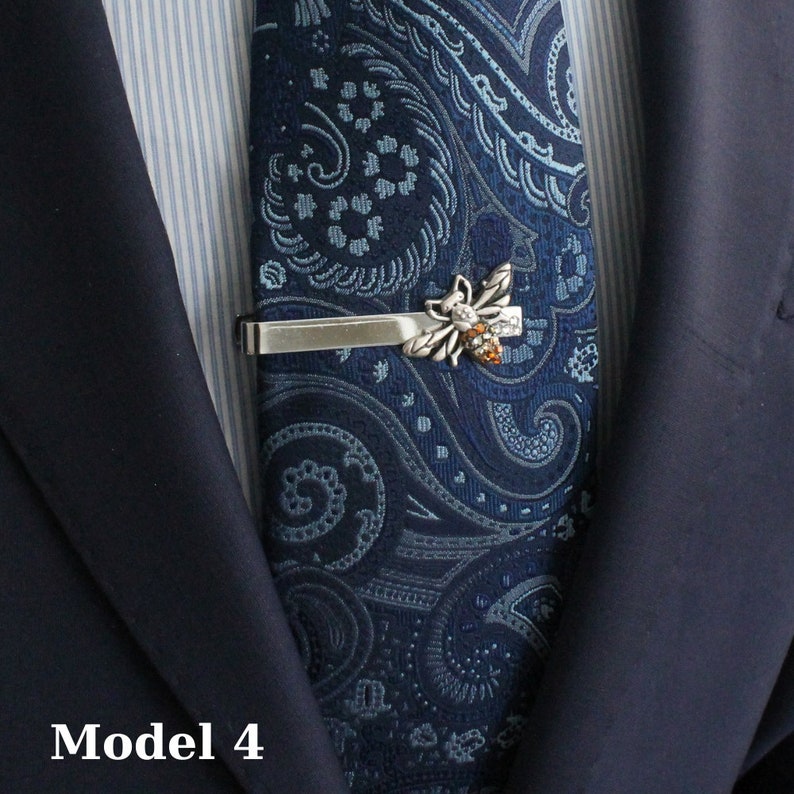 May include: Silver-toned tie clip featuring a detailed bee design with amber-colored accents. The clip is set against a navy blue paisley patterned tie, worn with a navy suit jacket. The text "Model 4" is visible at the bottom.