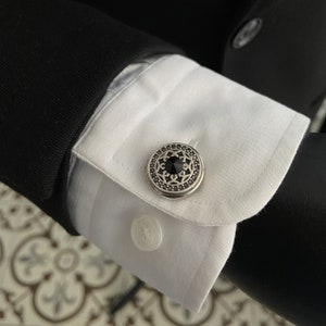 May include: Silver cufflinks with a black gemstone center and an intricate design.