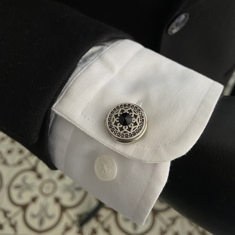 May include: Silver cufflinks with a black gemstone center and an intricate design.