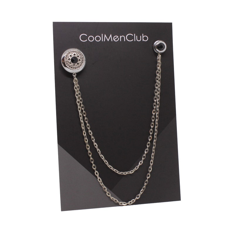 May include: Silver chain with a black stone and a decorative silver button. The chain is displayed on a black card with the text "CoolMenClub".