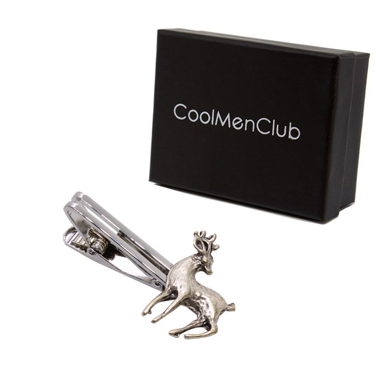 May include: A silver-toned tie clip featuring a detailed deer design. The clip is next to a black box with the text "CoolMenClub" in white. The deer has an antique finish, and the clip has a classic, functional design.