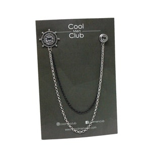 May include: A silver and black chain with a silver compass charm. The chain is attached to a black card with the text "Cool Men Club" printed on it.
