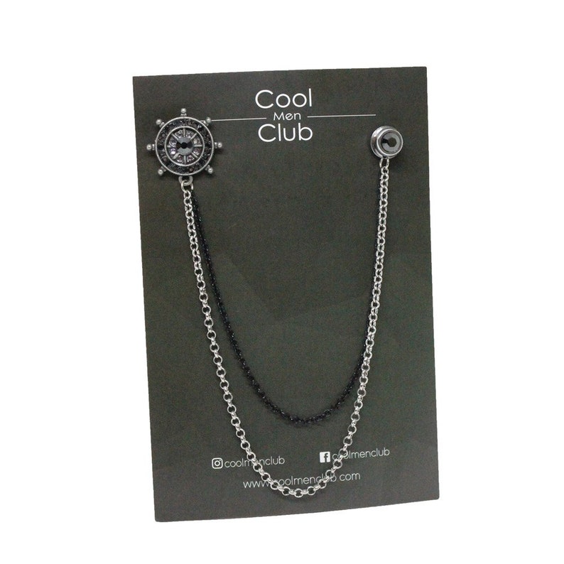 May include: A silver and black chain with a silver compass charm. The chain is attached to a black card with the text "Cool Men Club" printed on it.