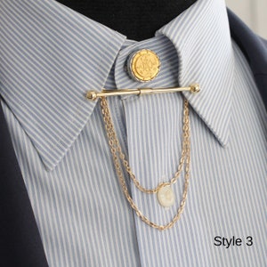 Pode incluir: Um alfinete de colarinho dourado com um topo decorativo em forma de moeda e correntes penduradas. O alfinete &eacute; preso a uma camisa listrada azul e branca. A imagem tamb&eacute;m inclui o texto "Style 3".