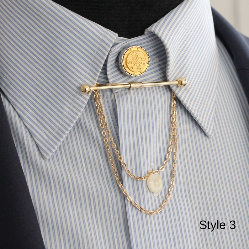Pode incluir: Um alfinete de colarinho dourado com um topo decorativo em forma de moeda e correntes penduradas. O alfinete &eacute; preso a uma camisa listrada azul e branca. A imagem tamb&eacute;m inclui o texto "Style 3".