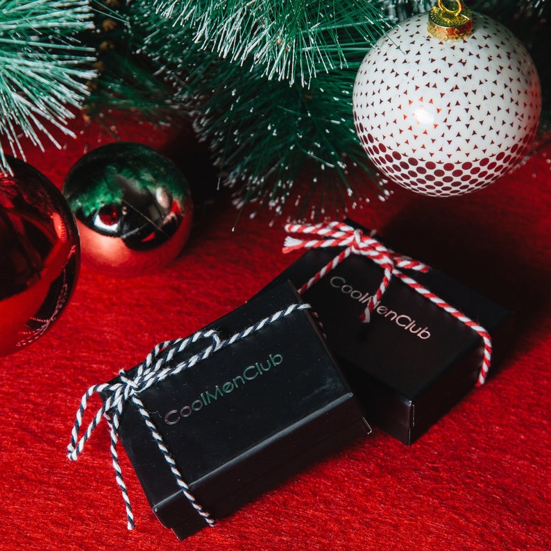 May include: Two black gift boxes with white and red string bows. The boxes are on a red surface and have the text "CoolMenClub" printed on them.