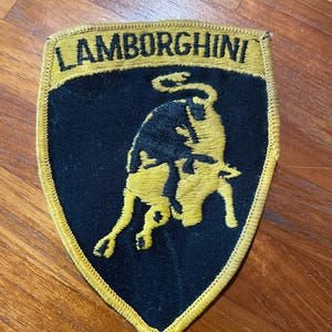 May include: A black and gold embroidered patch with the word "Lamborghini" and a charging bull logo.