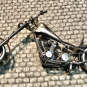 May include: A silver metal motorcycle model with a detailed engine and wheels. The motorcycle is on a gray textured surface.