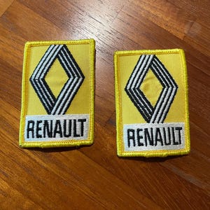 Op de afbeelding: Twee gele stoffen patches met een zwart-wit diamanten logo en het woord "RENAULT" in witte letters.