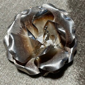 May include: A silver-toned metal rose brooch with a textured finish. The rose has a slightly oxidized look, giving it a vintage feel.