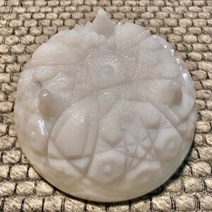 May include: White milk glass dish with a raised, geometric design. The dish has three feet and is perfect for serving snacks or desserts.