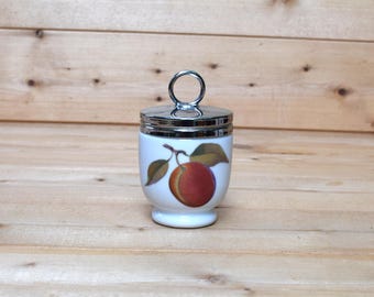May include: White ceramic egg cup with a silver lid and a single red plum with green leaves design.