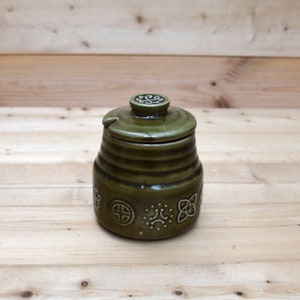 May include: A green ceramic sugar jar with a lid and a white Celtic knot design. The jar has a small spout for pouring.