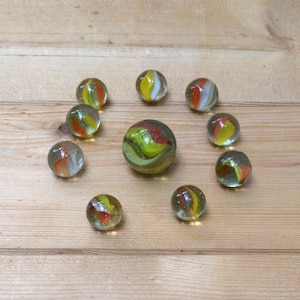 Peut inclure: Un ensemble de billes de verre colorées disposées sur une surface en bois. Les billes présentent des tourbillons de jaune, d'orange et de blanc à l'intérieur du verre transparent. Une bille plus grande est au centre, entourée de plus petites.