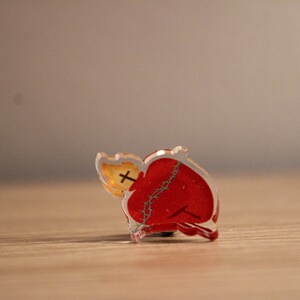 May include: A red heart with a crown of thorns and a flame on top, made of clear acrylic.