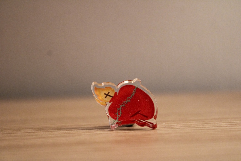 May include: A red heart with a crown of thorns and a flame on top, made of clear acrylic.