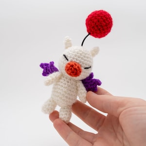 May include: A white crocheted plush toy with purple wings and a red balloon. The toy has a small orange nose and black eyes.